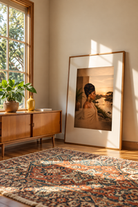 At The River earth-tone wall art in a wood frame on the floor beside a window and patterned rug